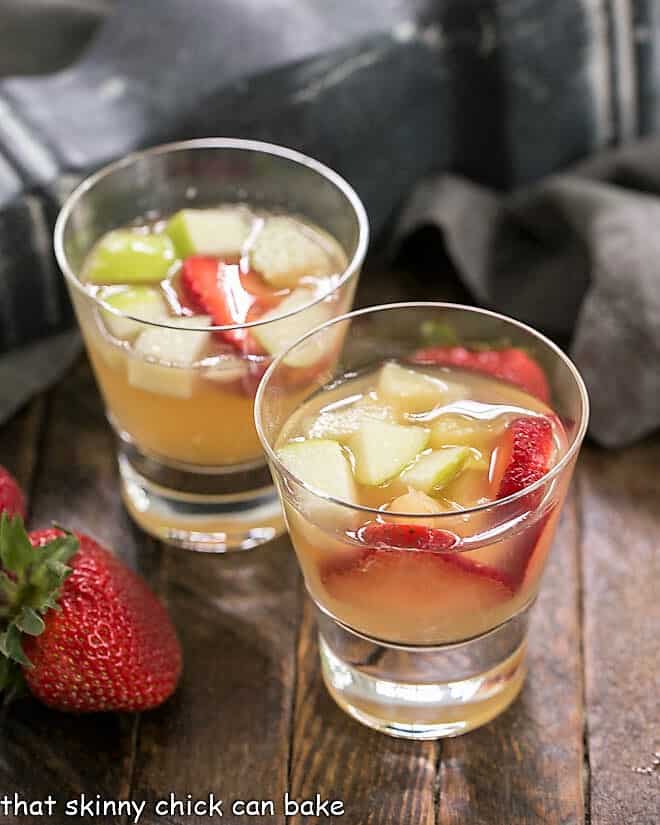 Two glasses of white wine sangria next to fresh strawberries.