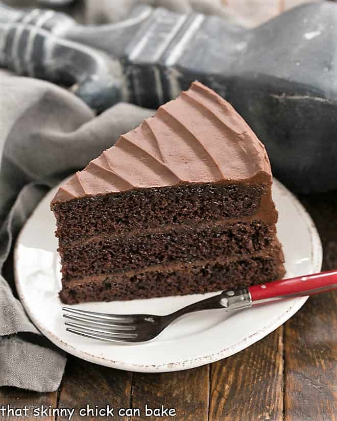 A slice of Hershey's Chocoate Cake on a white dessert plate with a red fork.