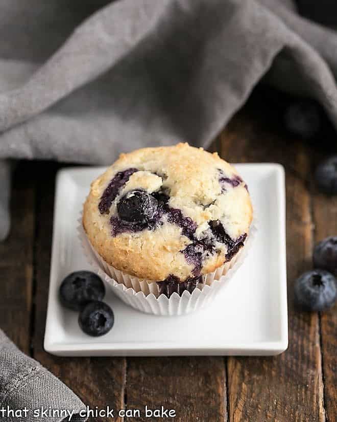 Blueberry Sour Cream Muffins on a white square plate with fresh blueberries