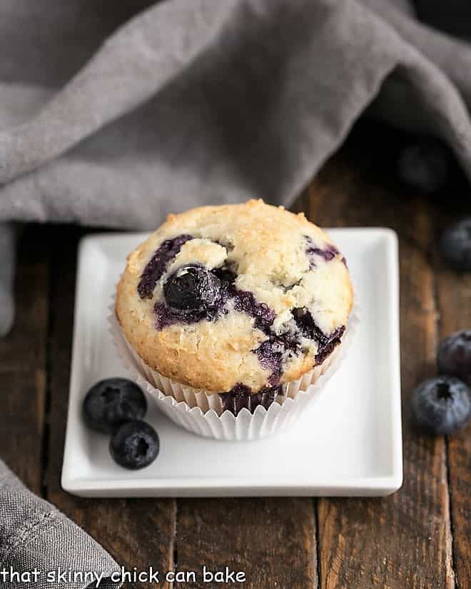 Blueberry Sour Cream Muffins on a white square plate with fresh blueberries.