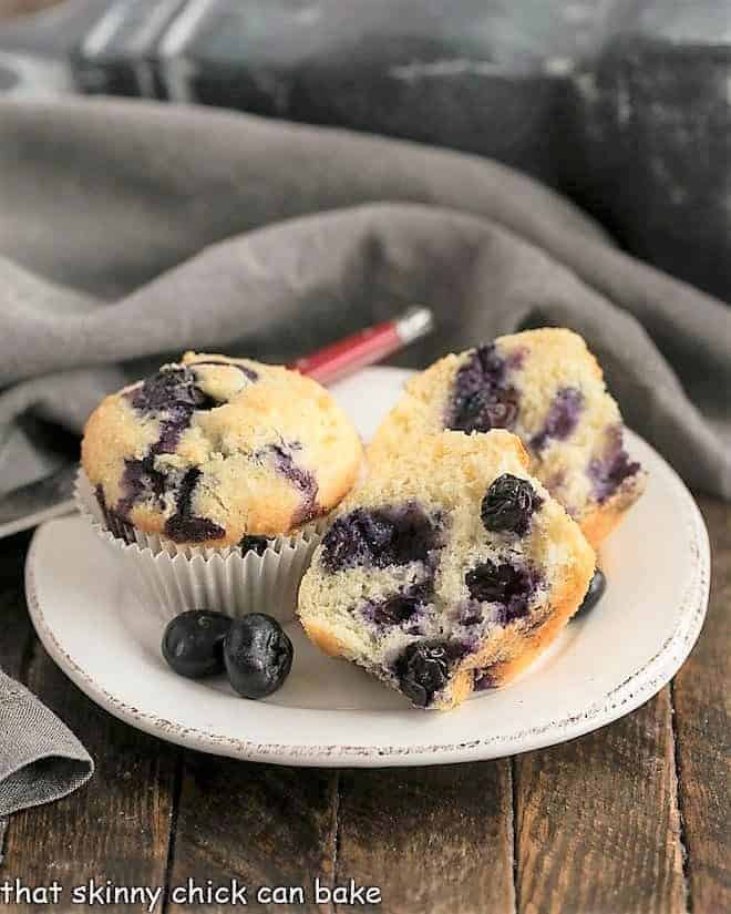 Blueberry Sour Cream Muffins on a round white plate with one cut to show the interior
