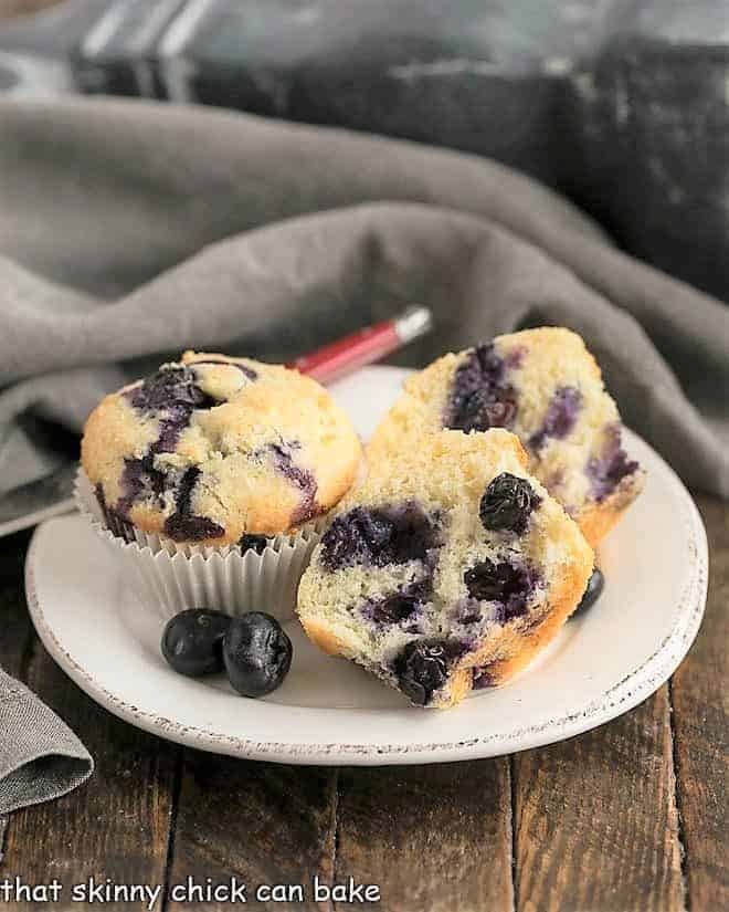 Blueberry Sour Cream Muffins on a round white plate with one cut to show the interior.