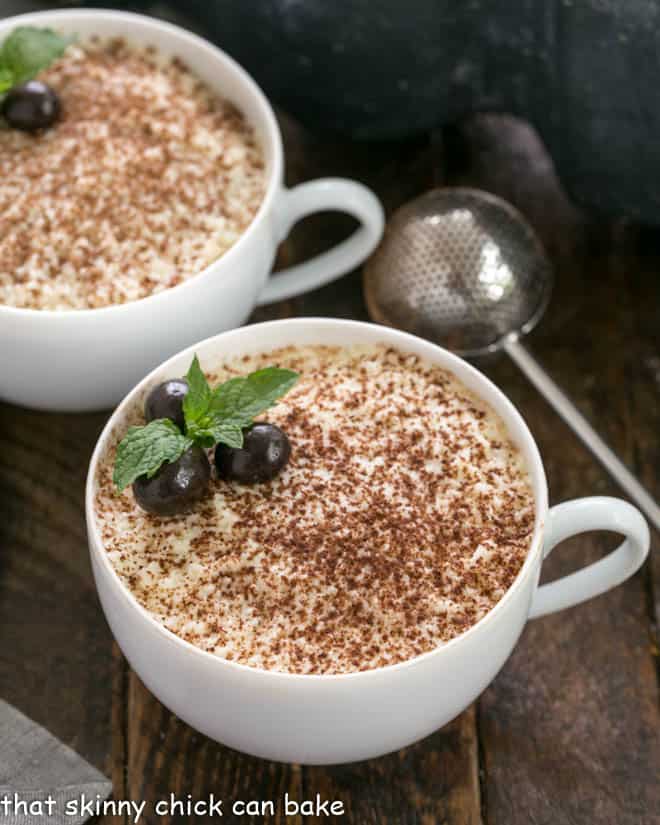 Two cups of chocolate tiramisu with a dusting wand full of cocoa powder.