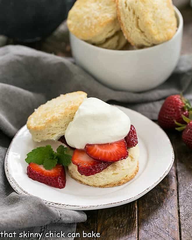 Classic strawberry shortcake on a plate in front of a bowl of shortcake biscuits.
