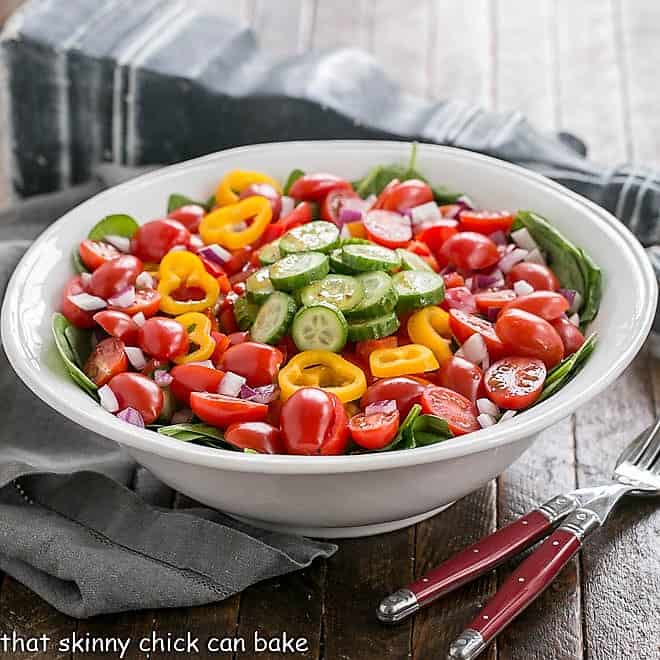 Gazpacho Spinach Salad in a white bowl with red-handled serving utensils.