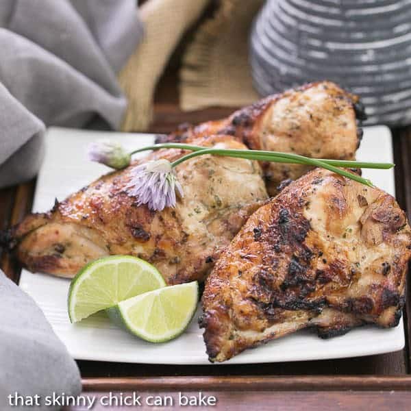 Grilled Thai Chicken on a square white plate with lime and chives.