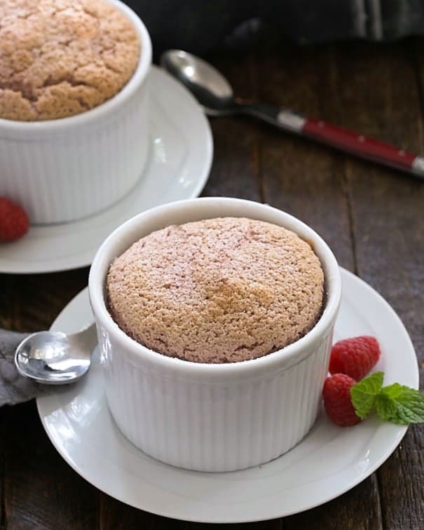 Two raspberry souffles on white dishes with spoons.