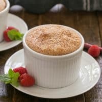 A raspberry souffle on a white plate with mint and raspberries to garnish