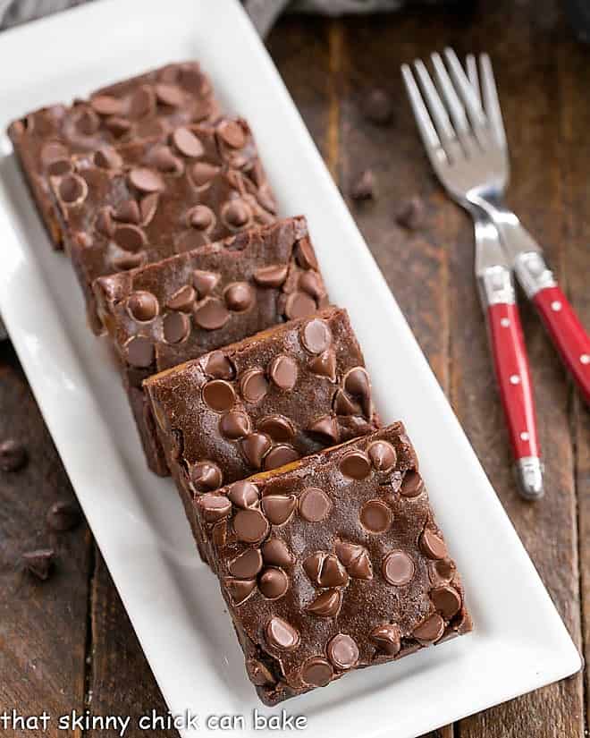 Overhead view of slices Caramel Brownieson a white rectangular tray with a couple of red handled forks