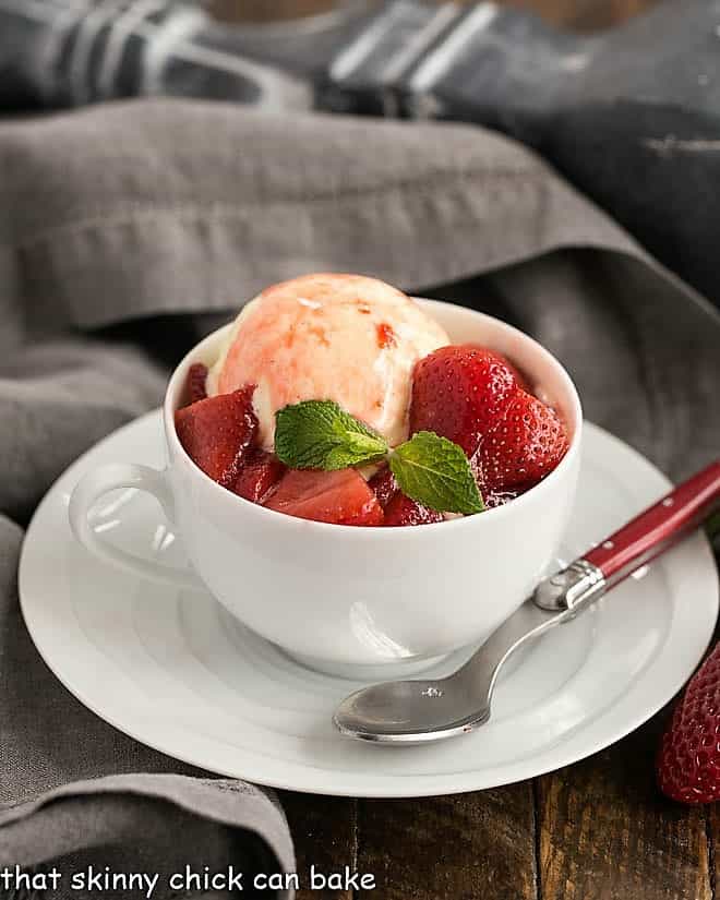 Cheesecake Ice Cream with Strawberry Sauce in a white teacup with a red handled spoon