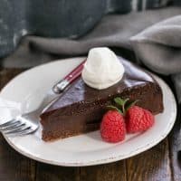 Slice of Flourless Chocolate Cake with Ganache Topping garnished with whipped cream and berries