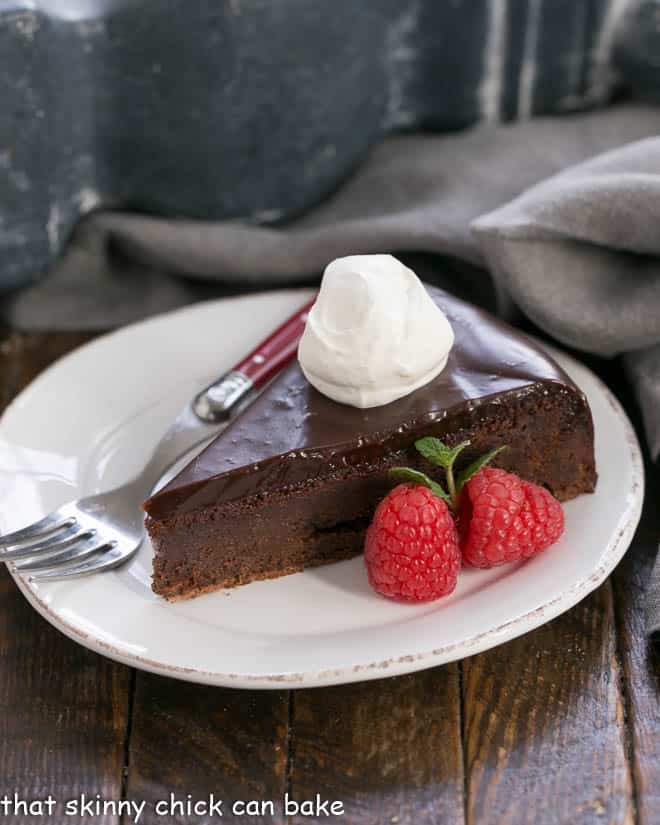 Slice of Flourless Chocolate Cake with Ganache Topping garnished with whipped cream and berries.