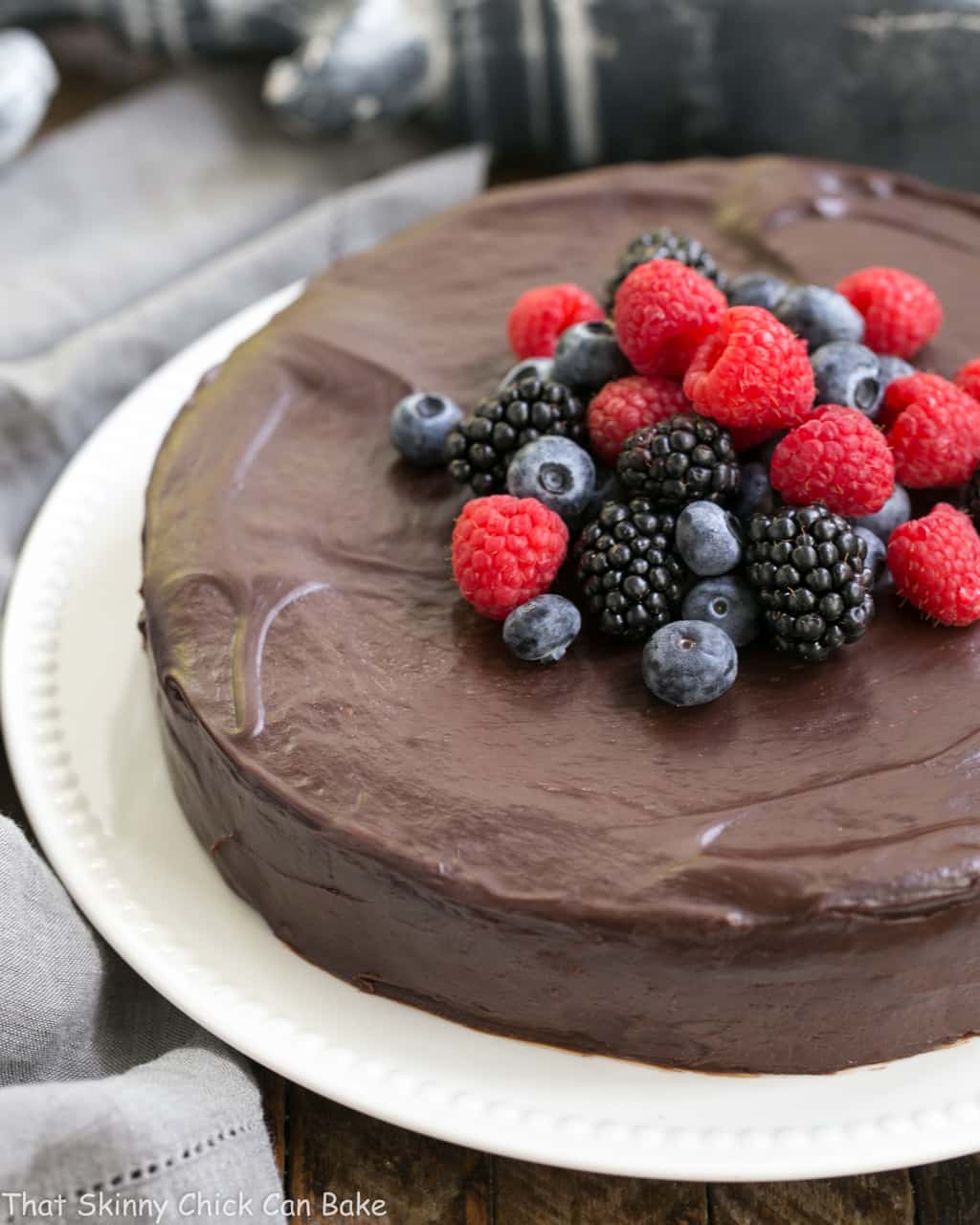 Flourless Chocolate Cake with Ganache Topping on a white plate topped with fresh berries.
