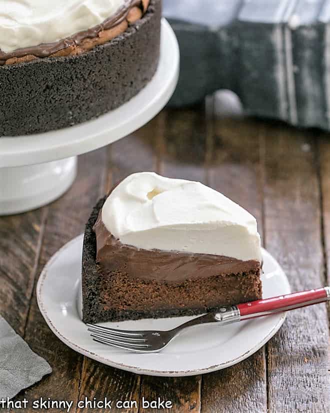 Mississippi Mud Pie Recipe - a decadent traditional mud pie recipe with an Oreo crust topped with a flourless chocolate cake, then silky chocolate pudding and whipped cream Slice of Mississippi Mud Pie in front of a cake stand.