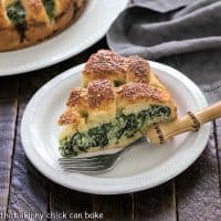 Slice of spinach torta rustica on a small white plate with a bamboo handled fork