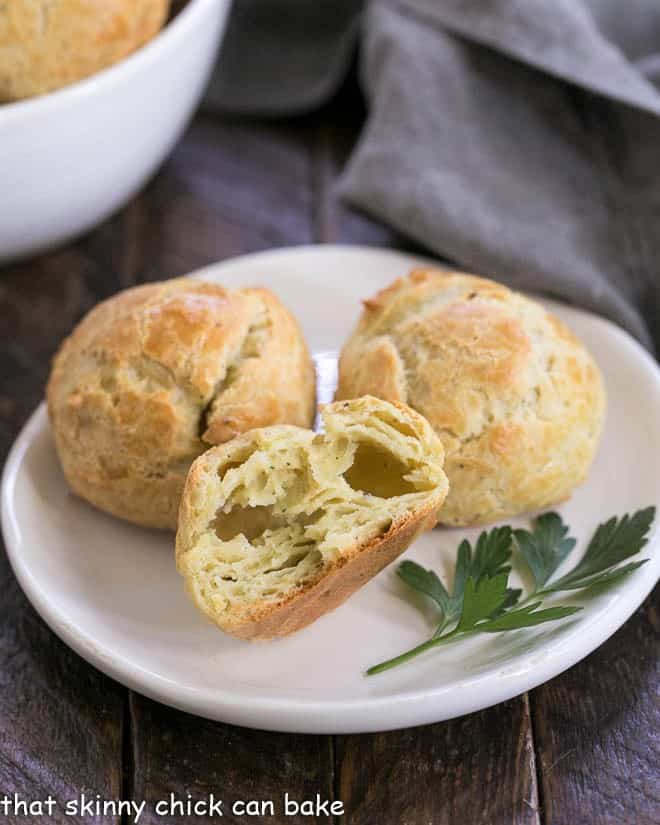 Cheese puffs on a small white place with one broken open to expose the interior.