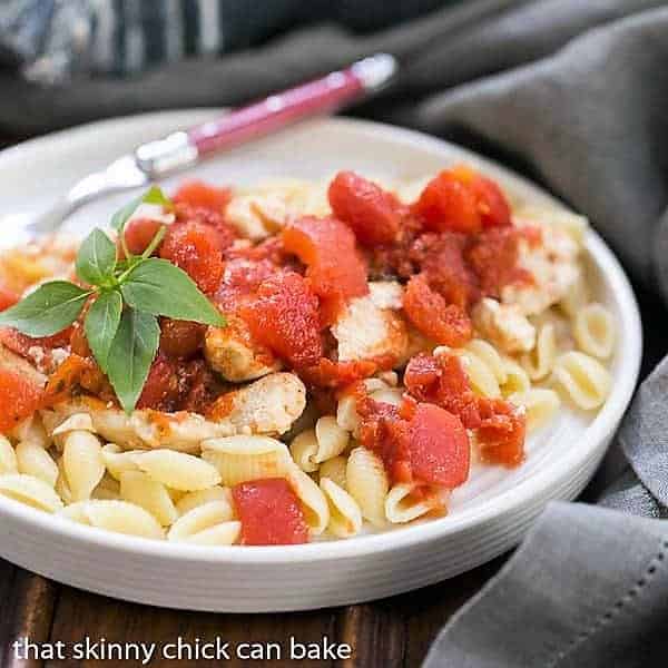 Chicken Feta Casserole - A fabulous casserole chock full of tomatoes, garlic, feta and herbs! Chicken Feta Casserole in a white bowl garnished with basil.