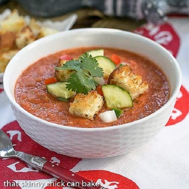 Classic Gazpacho with Homemade Croutons in a white ceramic bowl with a red handled spoon.