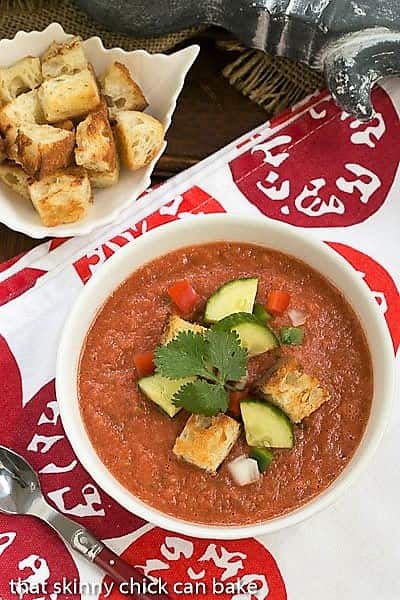 Overhead view of Classic Gazpacho with Homemade Croutons in a white bowl topped with cucumbers, peppers and croutons