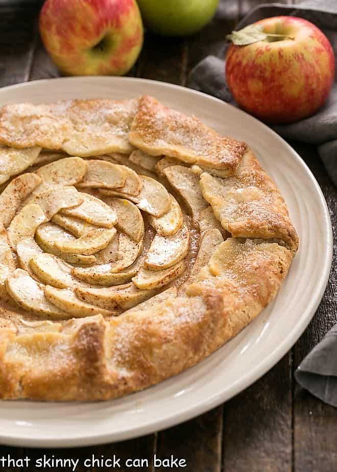 Rustic Apple Tart on a white plate with apples in the background.