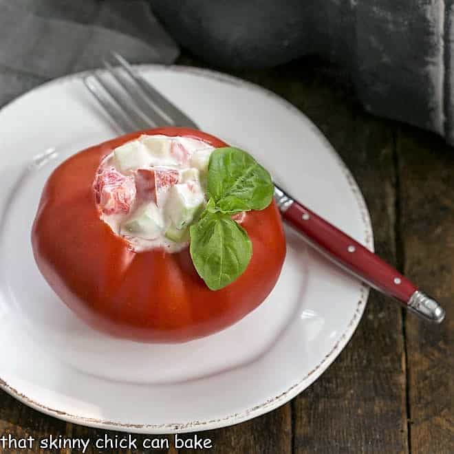 Stuffed tomato on a white plate with a red handle fork