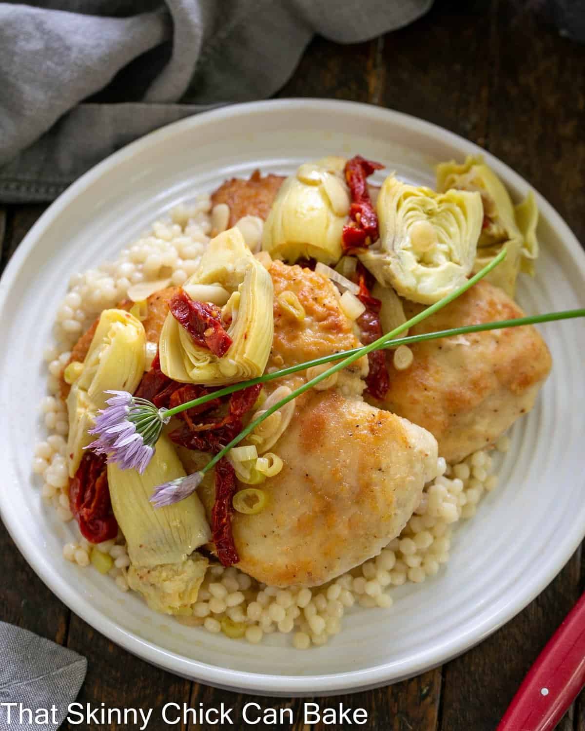 overhead view of chicken with artichokes on a white plate.