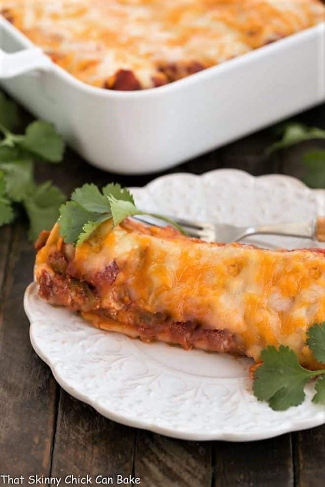 Cheesy Chicken Enchiladas - Spicy, cheesy at utterly irresistible Cheesy Chicken Enchiladas on a plate with a casserole dish in the background