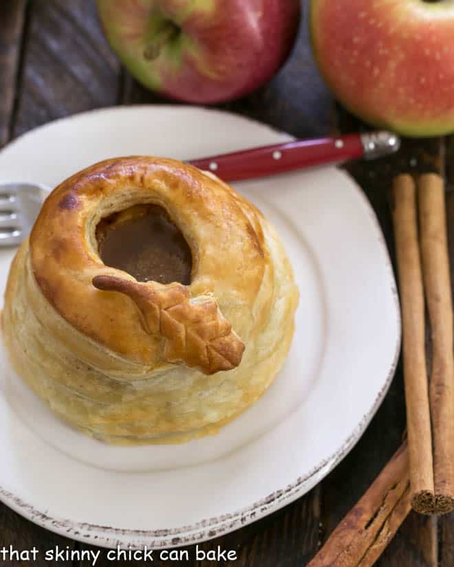 A pastry wrapped caramel apple on a white plate with a red handled fork