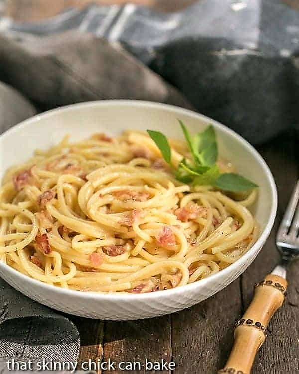 Classic Spaghetti Carbonara in a white bowl with a sprig of parsely