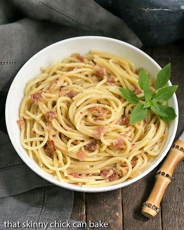 Overhead view of a bowl of spaghetti carbonara with a basil sprig garnish.