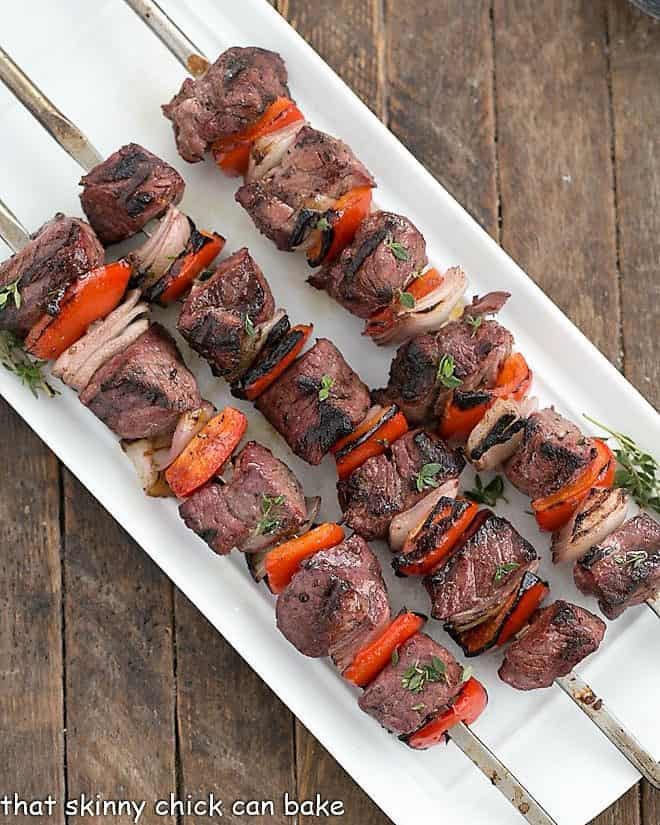 Marinated Greek Lamb Kebabs skewered on a white ceramic tray viewed from above.