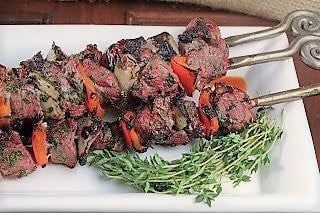 Greek kabobs on a white tray with thyme