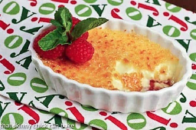 Creme brulee with raspberries in a  white dish topped with fresh raspberries and mint