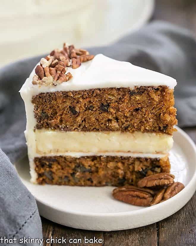 Slice of Cheesecake Filled Carrot Cake on a rimmed white plate with pecans