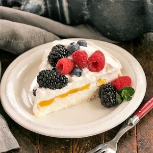 Slice of lemon Pavlova topped with berries on a white dessert plate