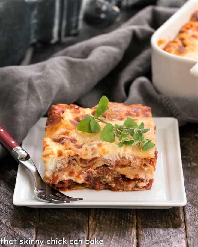 A slice of Sausage Ricotta Lasagna on a white plate with a sprig of oregano.