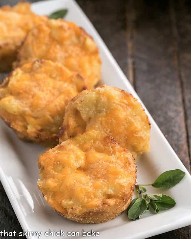 Close view of cheesy potato cups on a ceramic platter with a spig of oregano.