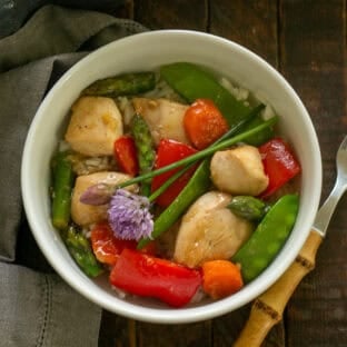 Chicken Stir Fry in a white bowl with chive garnish and a fork.