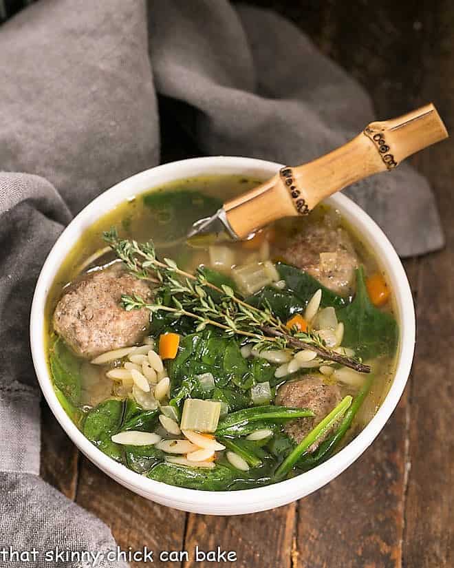 Overhead view of a bowl of Italian Wedding soup with a bamboo handled spoon holding a meatball.