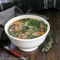 Italian wedding soup in a white bowl with a sprig of thyme