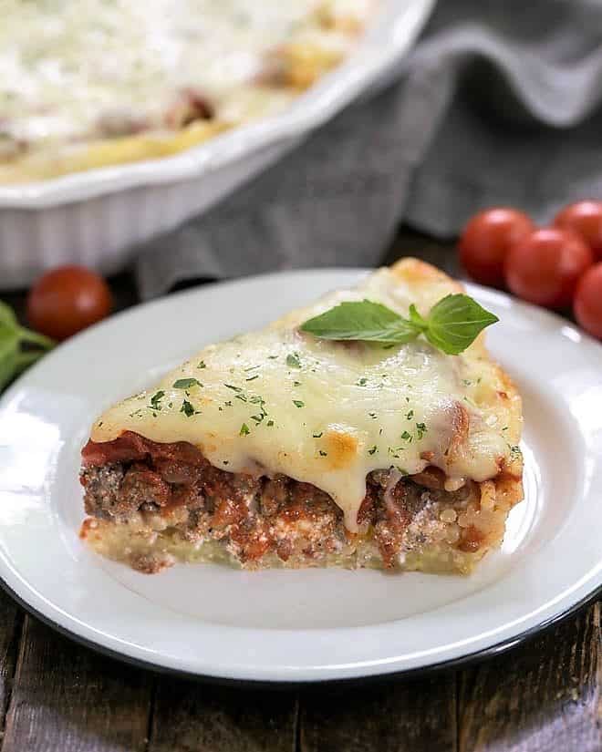 Slice of spaghetti pie topped with a sprig of basil on a white plate