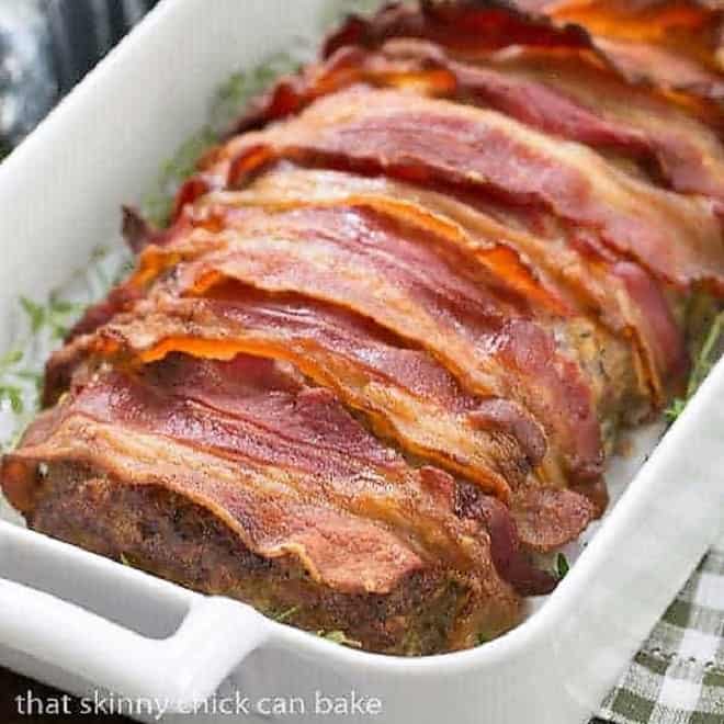 Bacon Wrapped Meatloaf in a white casserole dish garnished with fresh thyme.