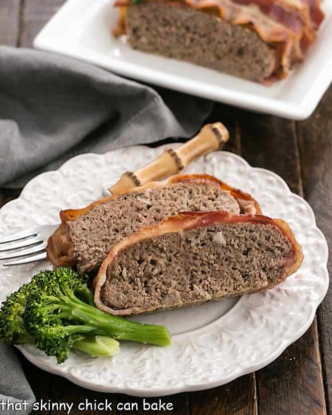 A plate with sliced meatloaf in front of a tray of meatloaf.