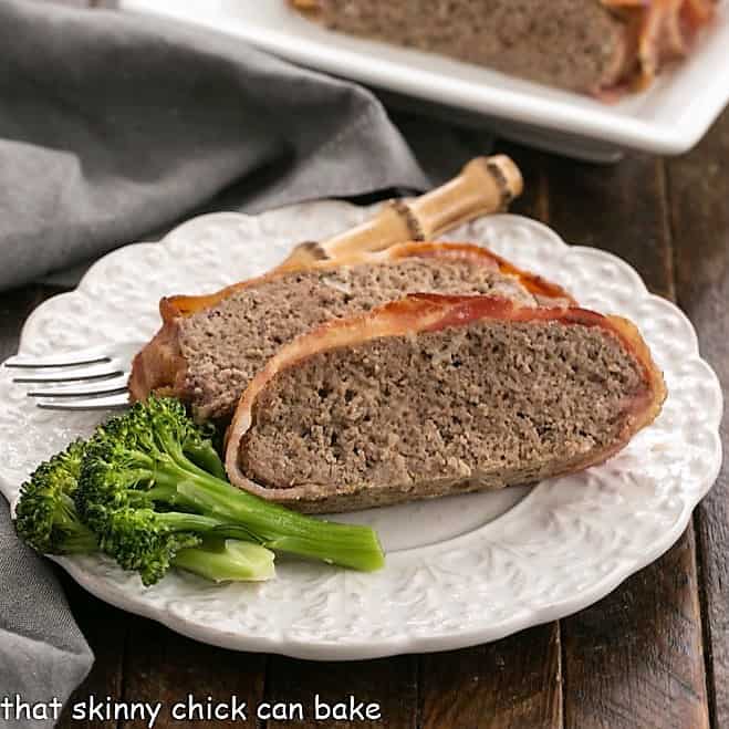 Bacon wrapped meatloaf slices on a white dinner plate with a fork and two broccoli spears