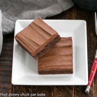 2 cocoa brownies on a square white plate with a red handle fork