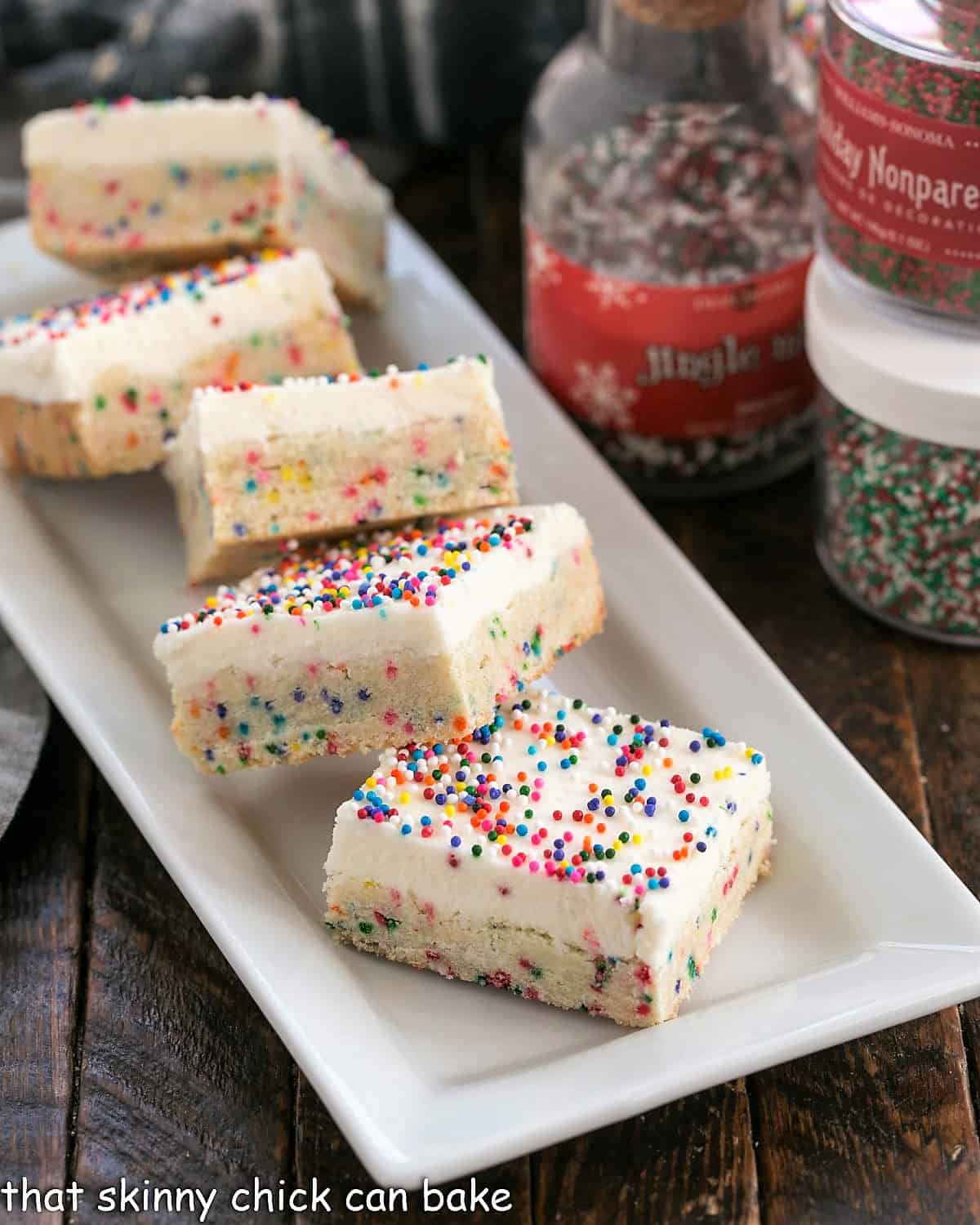 Frosted Sugar Cookie Bars on a white ceramic tray with jars of sprinkles.