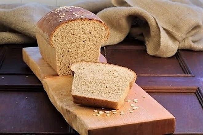 Sliced loaf of Honey Oatmeal Bread on a wooden cutting board