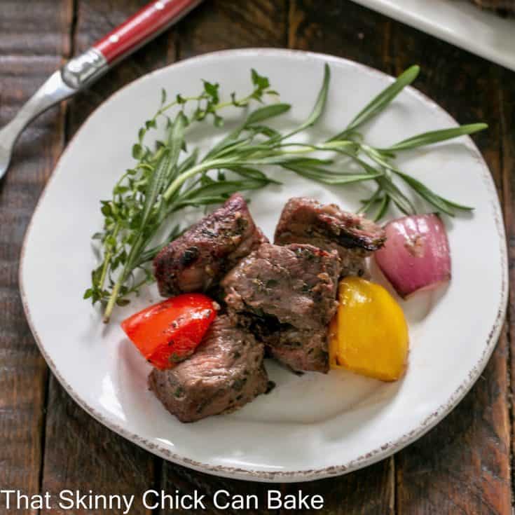 Small white plate with pieces of grilled lamb and vegetables with a herb garnish