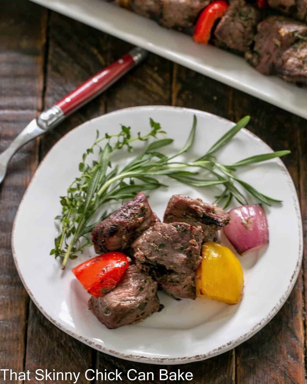 Overhead view of lamb off the skewers on a round white plate with herbs.