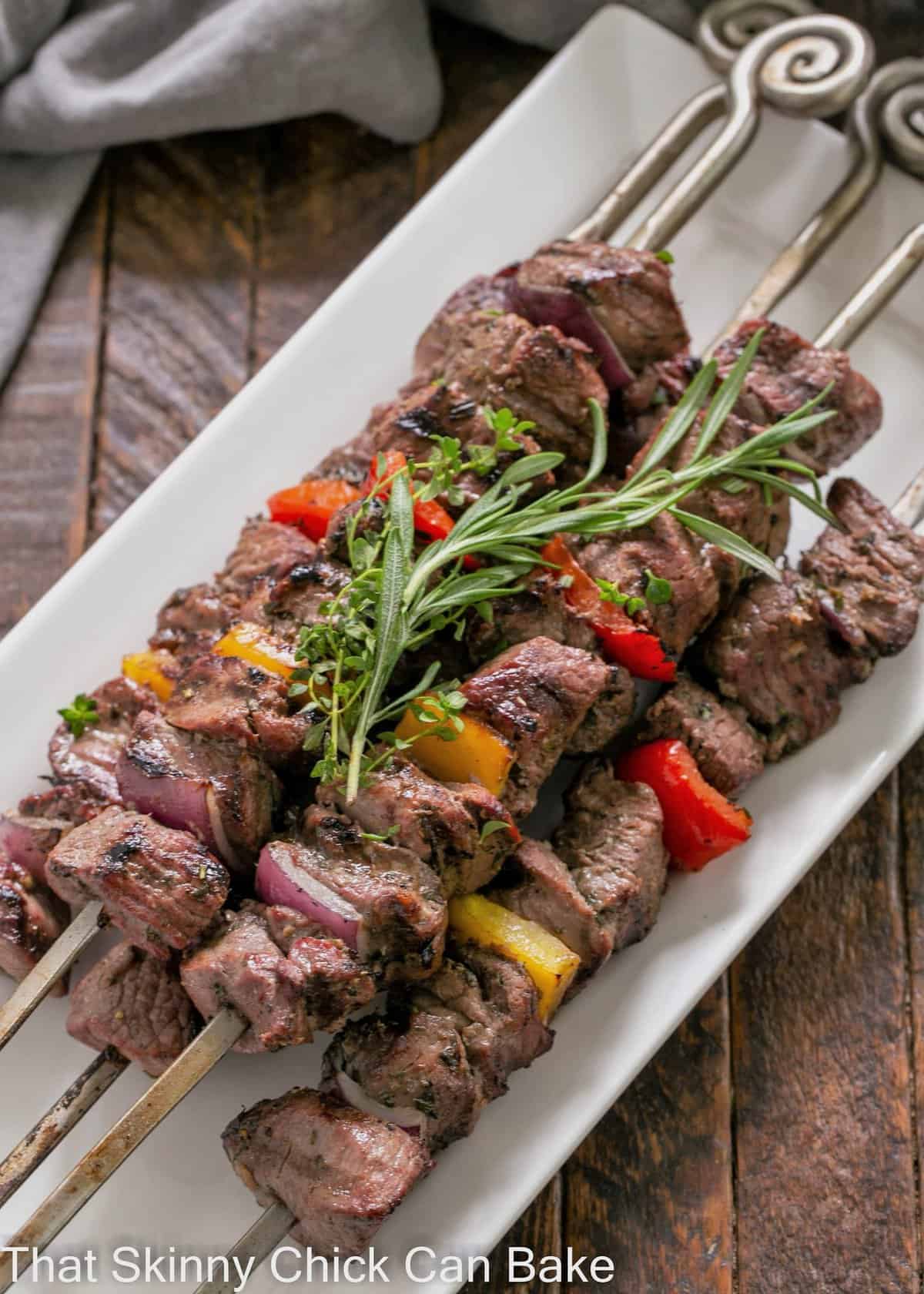 Overhead view of lamb kabobs on a white platter with an herb garnish.